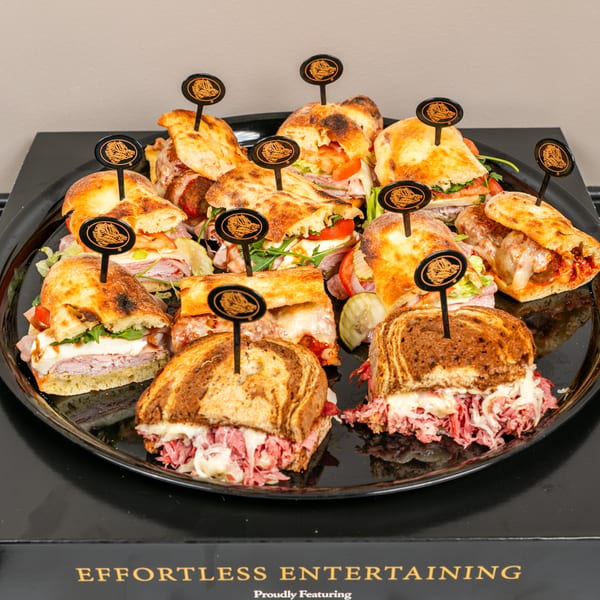 A black platter filled with various sandwiches, including Reubens, meatball subs, and Italian subs.