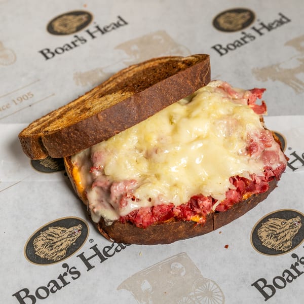 Boar's Head deli sandwich with melted cheese and corned beef on toasted dark bread.
