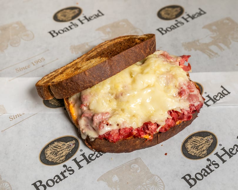 Boar's Head deli sandwich with melted cheese and corned beef on toasted dark bread.