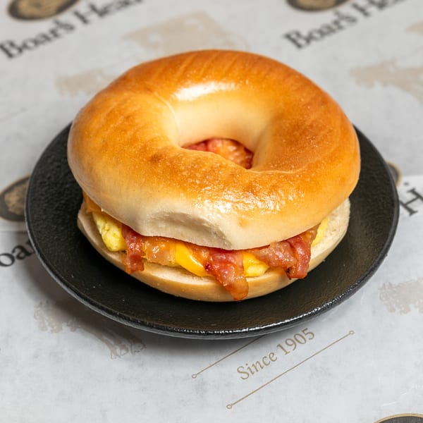 A bacon, egg, and cheese bagel sandwich on a black plate, with "Boar's Head" paper underneath.