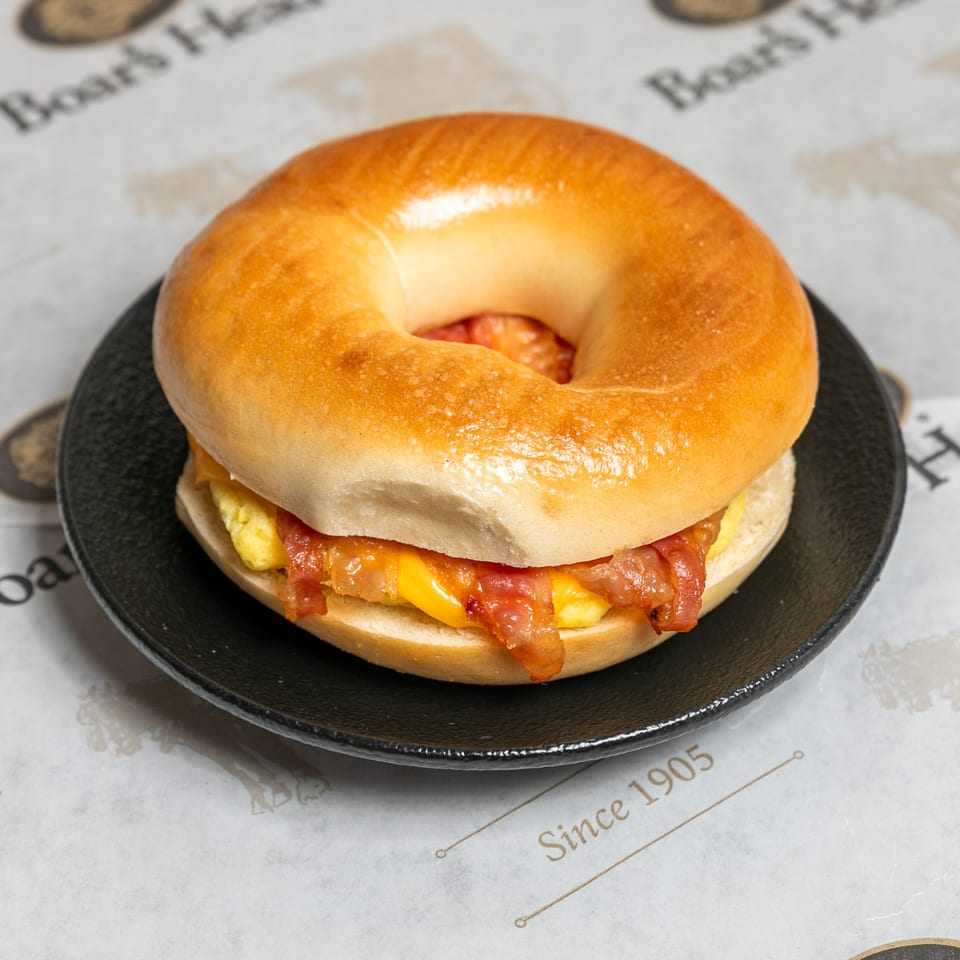 A bacon, egg, and cheese bagel sandwich on a black plate, with "Boar's Head" paper underneath.