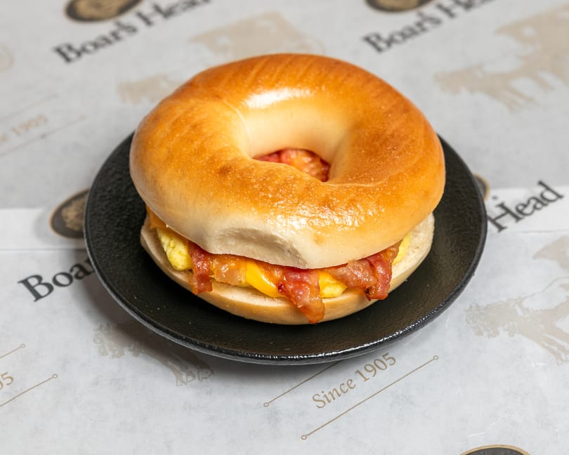 A bacon, egg, and cheese bagel sandwich on a black plate, with "Boar's Head" paper underneath.