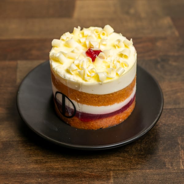 Layered dessert with white chocolate curls and a red jelly center on a black plate.