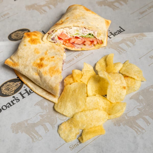 Boar's Head wrap, cut in half, filled with meat, cheese, and vegetables, served with potato chips.