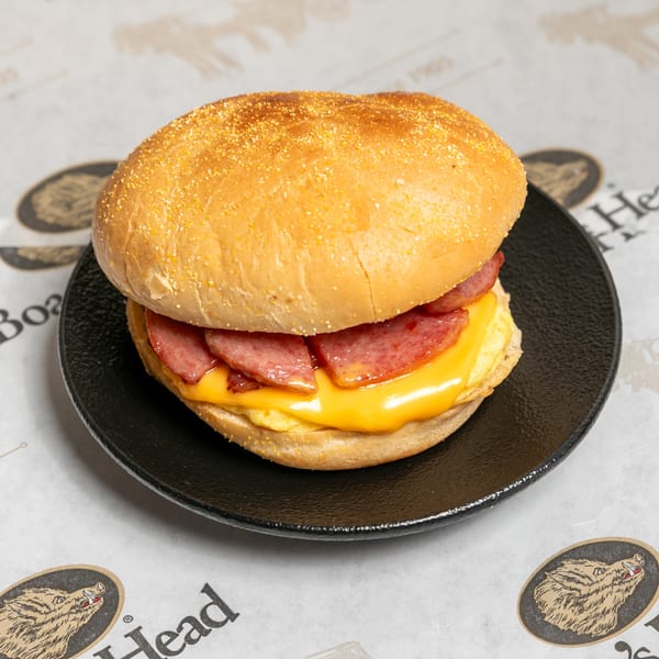 A breakfast sandwich with sausage, melted cheese, and egg on a bun, on a black plate.