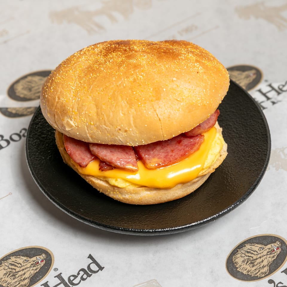 A breakfast sandwich with sausage, melted cheese, and egg on a bun, on a black plate.