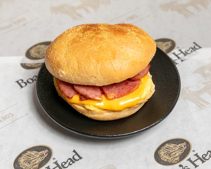 A breakfast sandwich with sausage, melted cheese, and egg on a bun, on a black plate.
