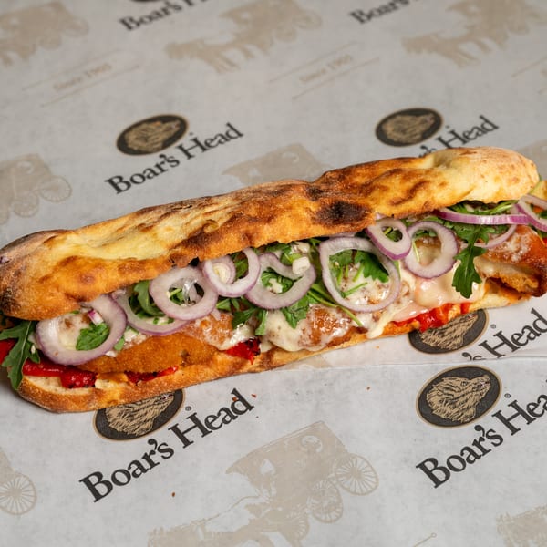 A Boar's Head sandwich with crispy chicken, melted cheese, red onions, and arugula on flatbread.